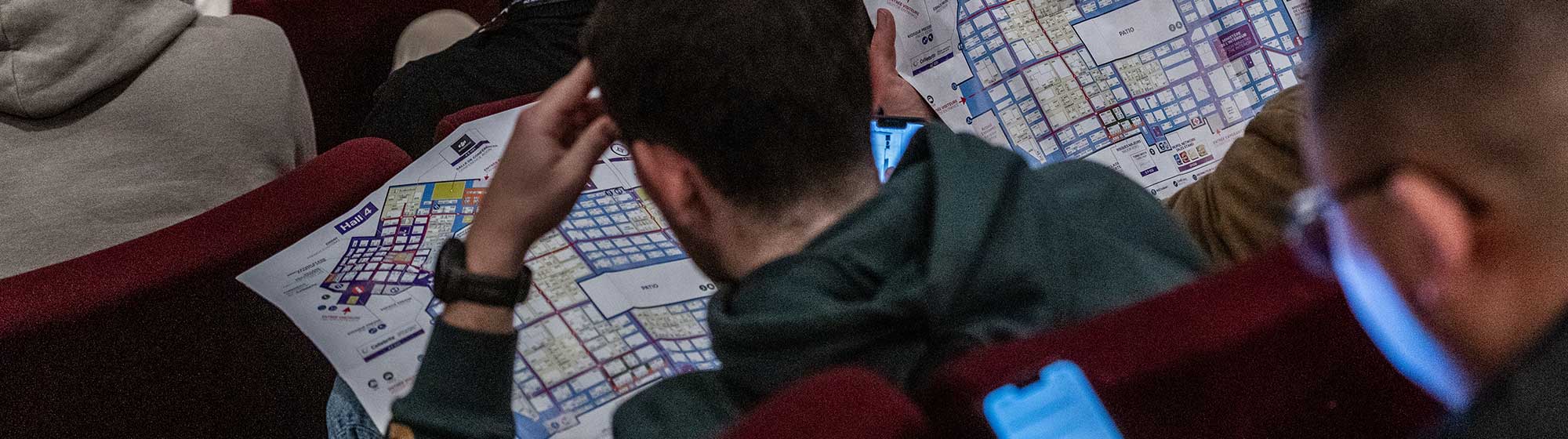Two men consult a Milipol Paris map sitting in an auditorium full of people