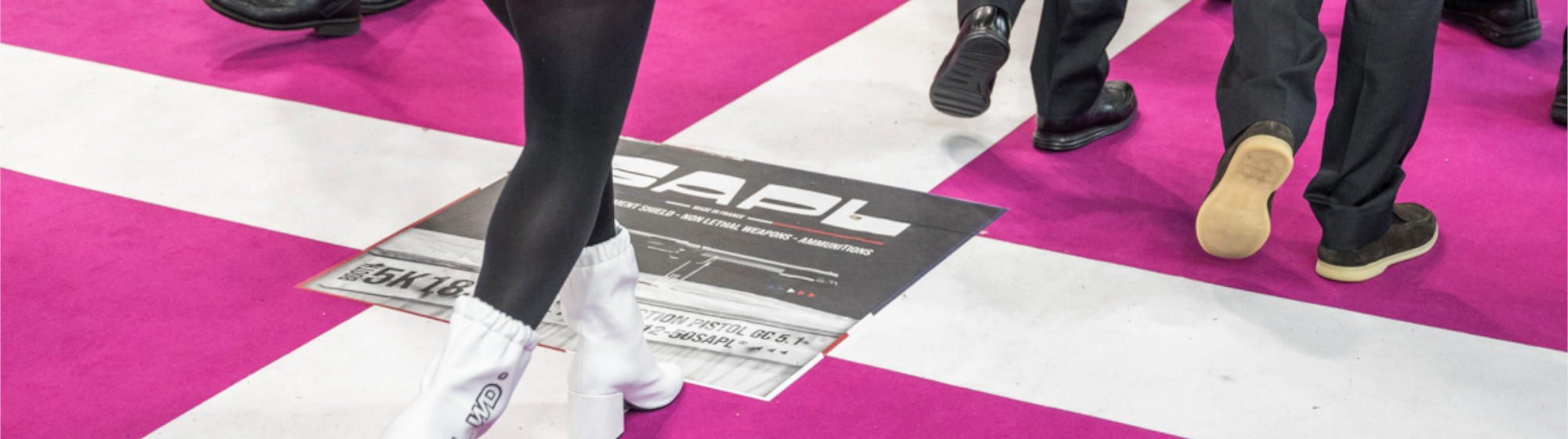 Visitors at Milipol Paris walking in the aisle with an exhibitor signage on the floor