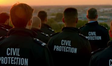Groupe de membres de la Protection Civile observant le paysage au coucher du soleil, avec leurs vestes portant l'inscription "PROTECTION CIVILE".