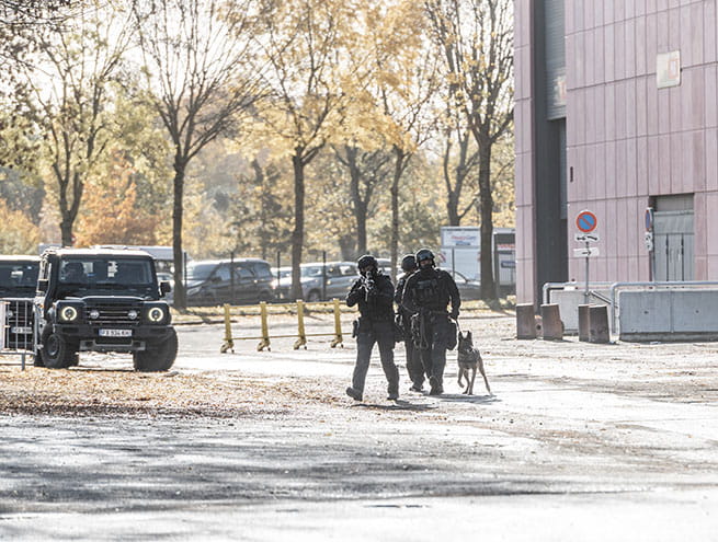 RAID police officers with a dog near a building and a vehicle