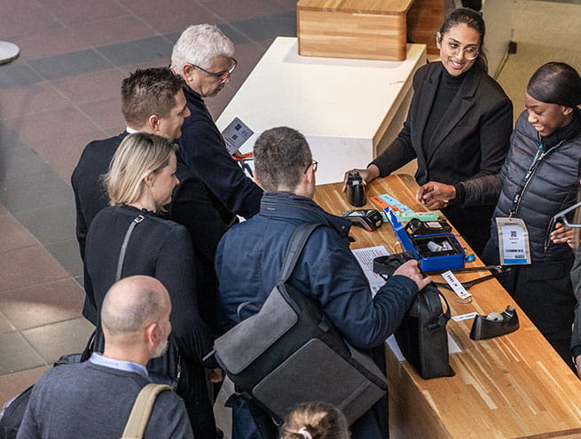 A group of people, are gathered around a registration desk receiving materials and badges from staff