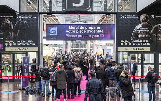 Hall entrée visiteurs bondé avec affiche Milipol de bienvenu et deux grandes affiches publicitaires MEHLER SYSTEMS, une société qui fournit des solutions pour la protection balistique.