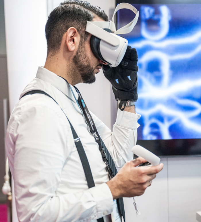 Man in a white shirt testing a virtual reality headset and connected gloves at an exhibition booth.